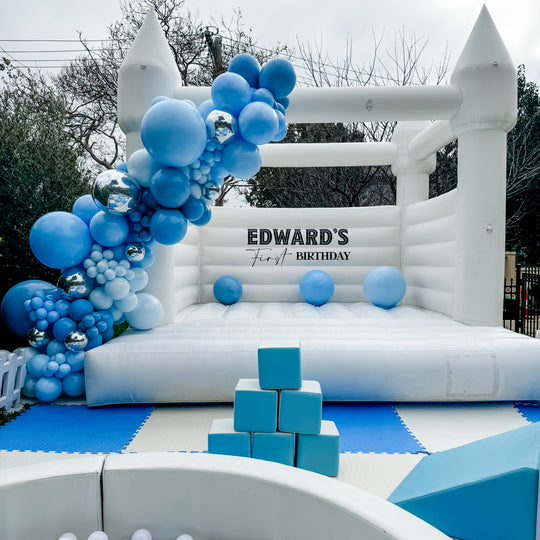 Edward balloon garland in shades of blue and chrome silver on a white bouncy castle in a garden for party hire in Melbourne