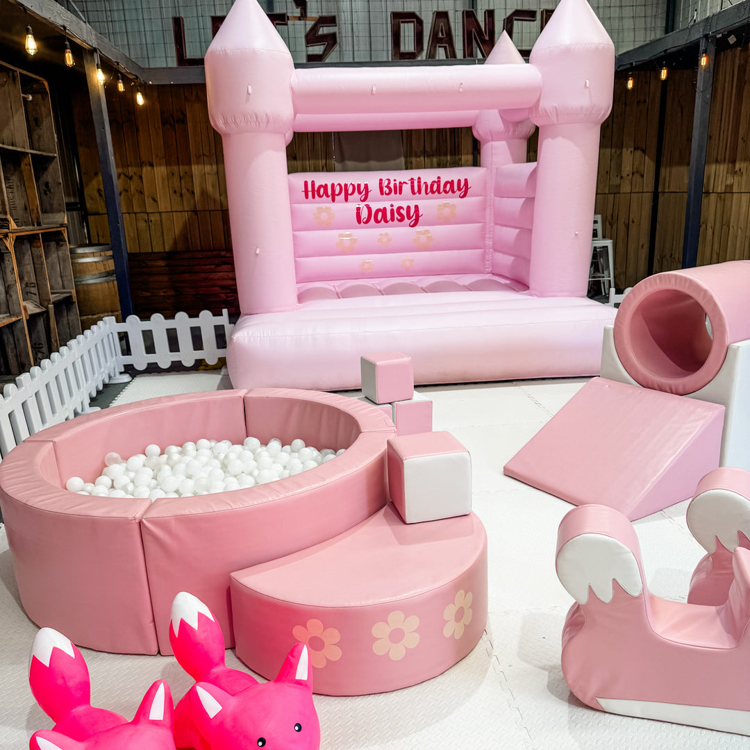 Dusty pink ball pit with white balls, a floral step, blocks, tunnel and slide by a pink castle reading Happy Birthday Daisy