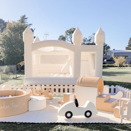 Tan soft play with a round ball pit, white car and ring tunnel in front of a white castle on a lawn for party hire in Melbourne