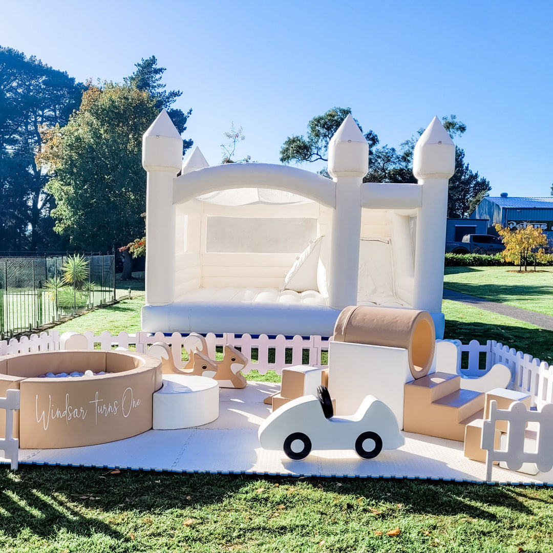 Tan ball pit reading Windsar Turns One with a white car, tunnel and fox rockers fenced in front of a white castle with a slide