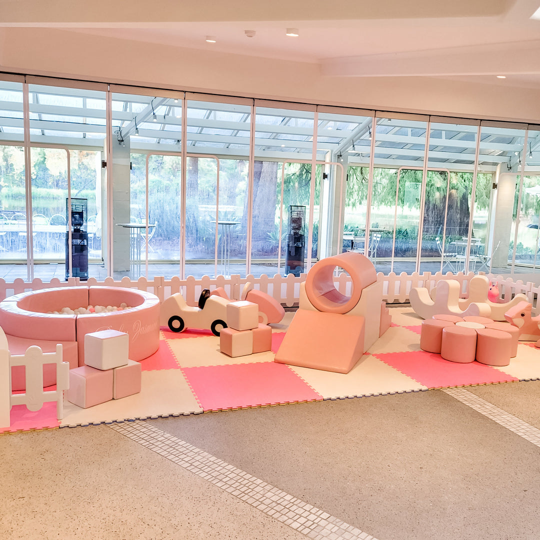 Front view of the baby pink soft play with a Baby Jasmine ball pit, blocks, foam cars, ring tunnel and flower seat on pink mats