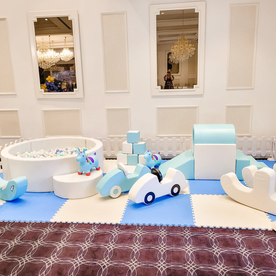 Close view of the baby blue and white foam cars, unicorn hoppers, blocks and round ball pit on blue and white mats in a ballroom