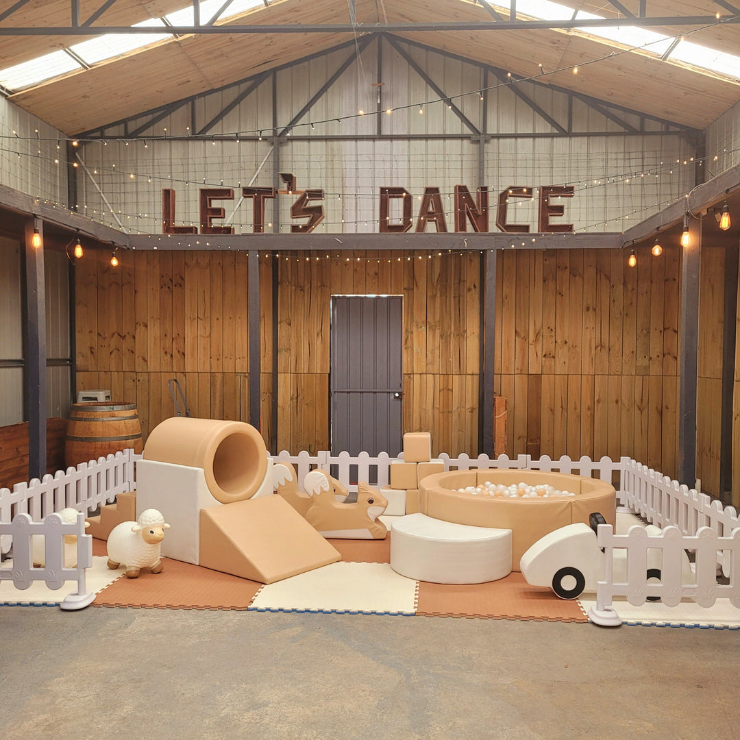 Tan soft play set inside a white picket fence in a rustic warehouse venue with a Let's Dance sign and festoon lights overhead