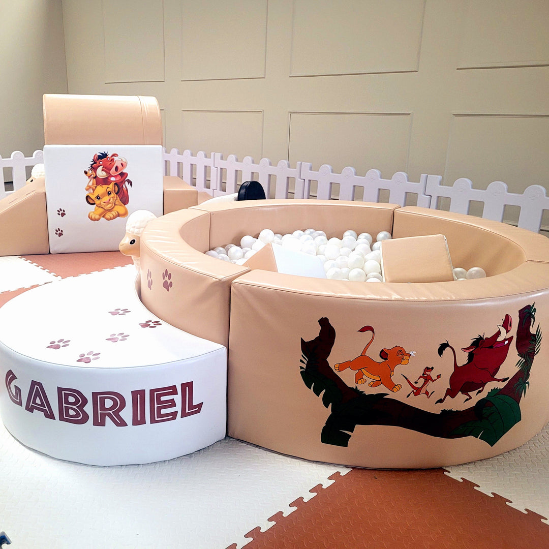 Close-up of the Lion King Simba, Timon and Pumbaa decal on the tan ball pit next to a white half-moon step reading Gabriel