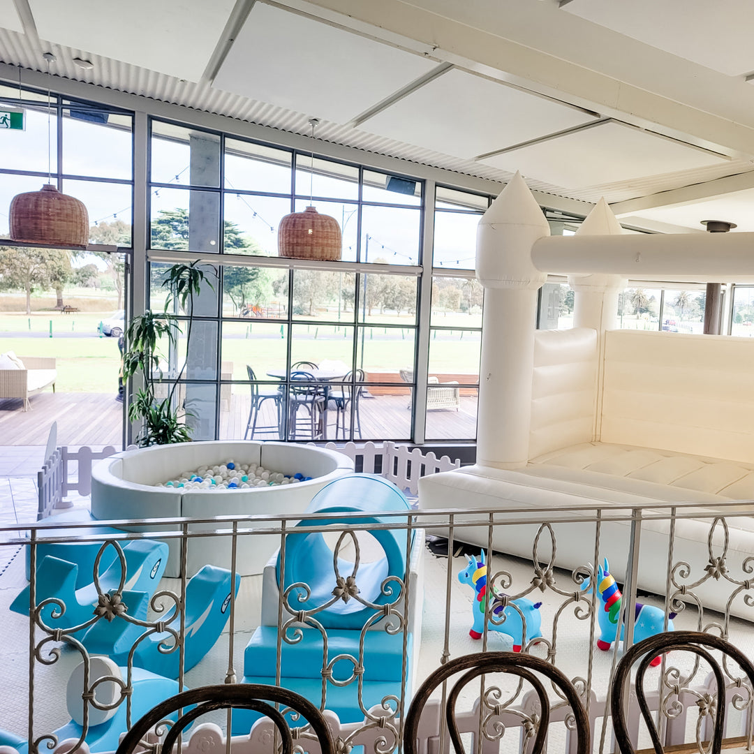 Baby blue soft play setup with ball pit, tunnel climber, whale rockers and unicorn hoppers seen over an iron railing