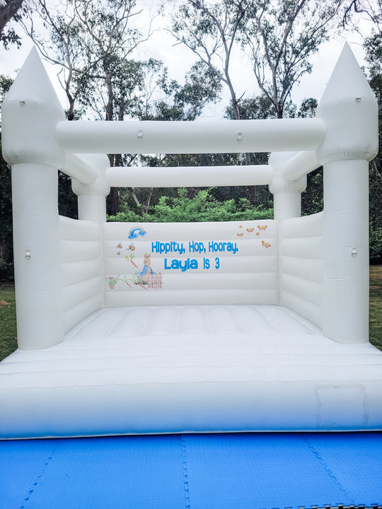 Peter Rabbit theme decal reading Hippity Hop Hooray Layla is 3 on the back wall of a white bouncy castle under gum trees