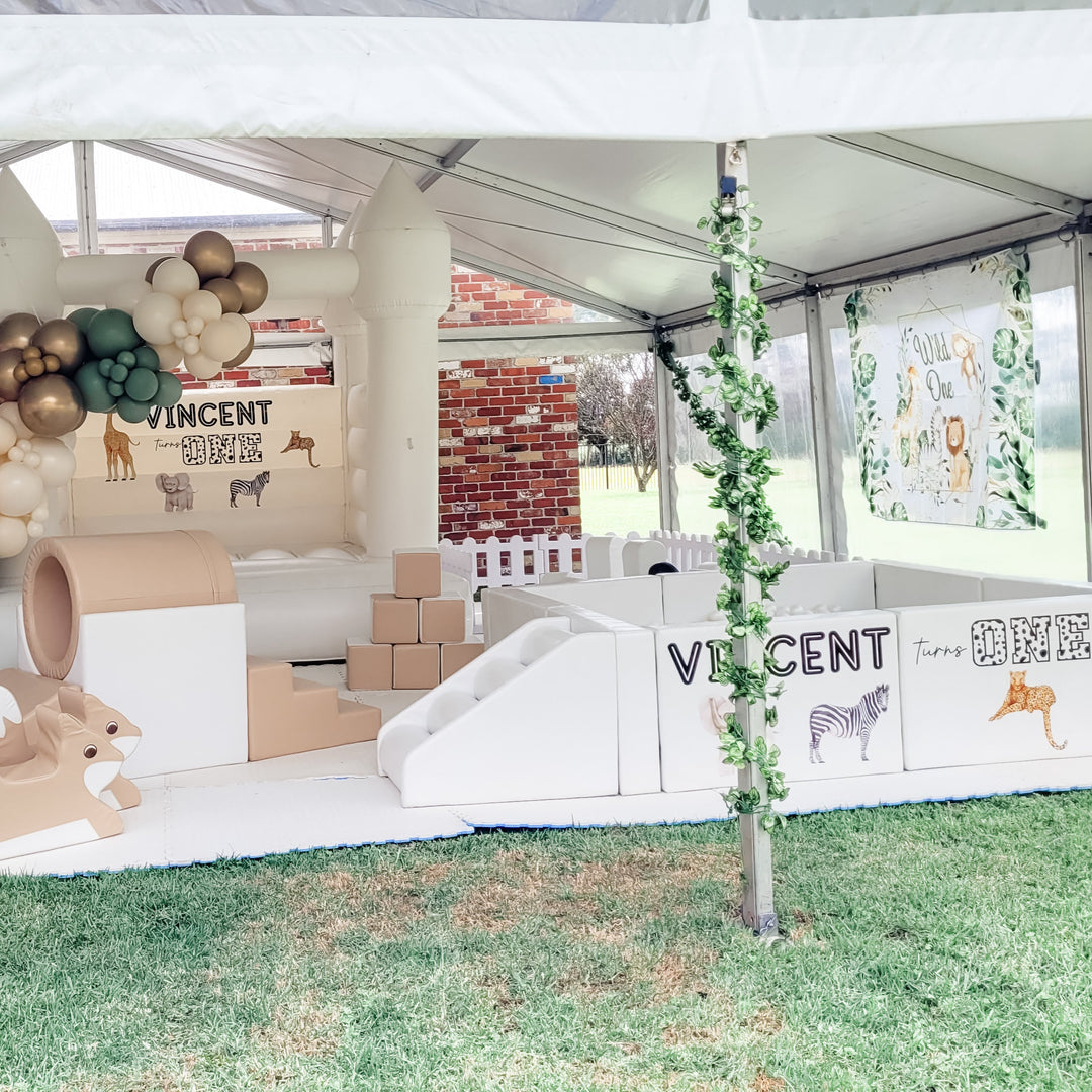 Safari themed tan soft play and ball pit reading Vincent turns One in a marquee, white castle with green balloons behind