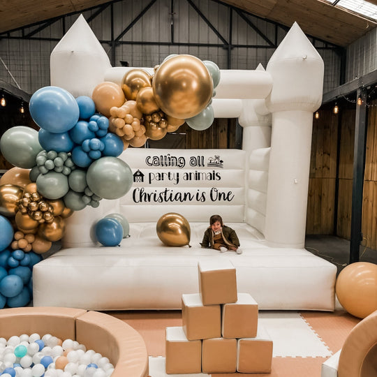 Christian balloon garland in blue, sage, tan and gold on a white bouncy castle with a toddler for party hire in Melbourne