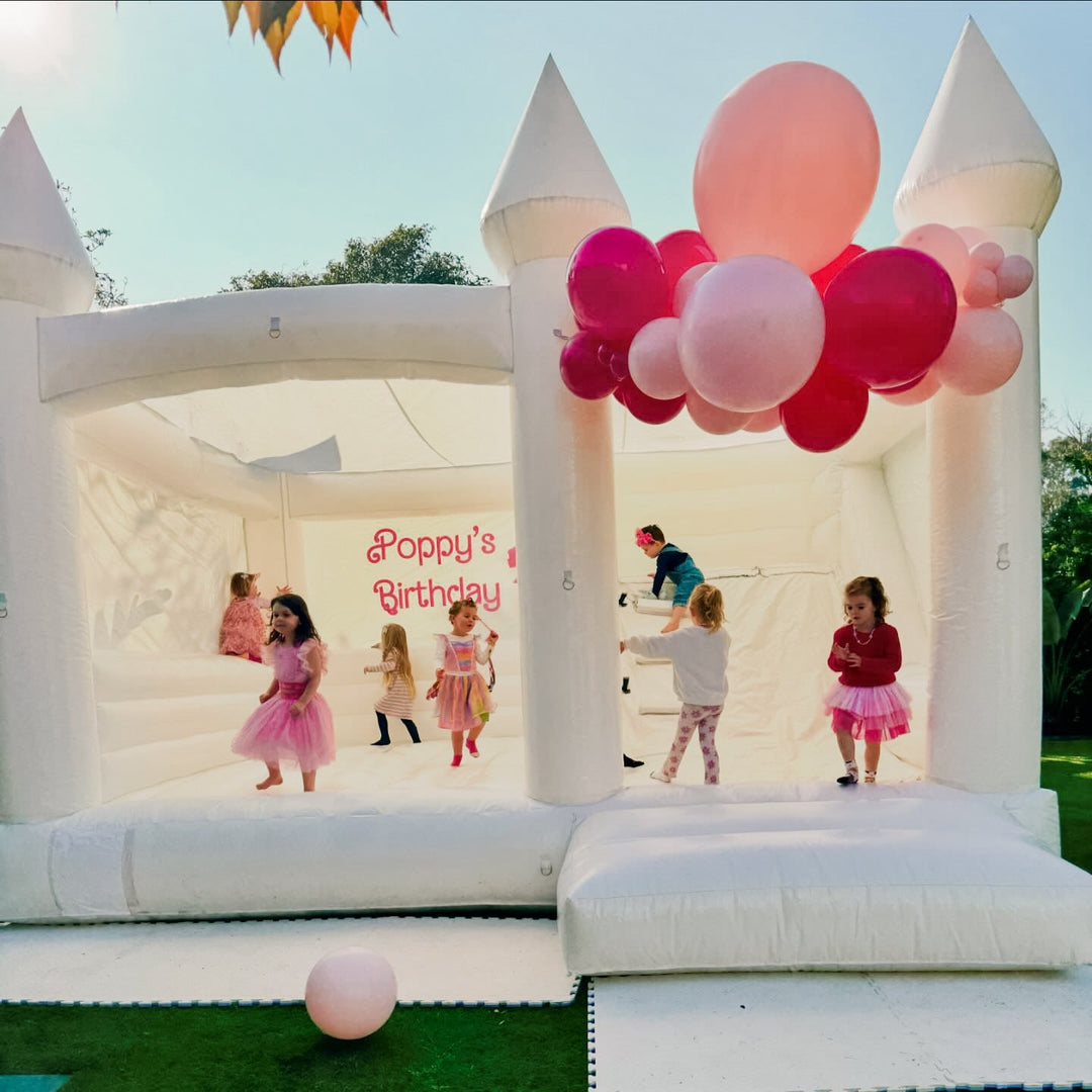 Children in party dresses bouncing inside the William white castle with slide under a pink and hot pink balloon garland