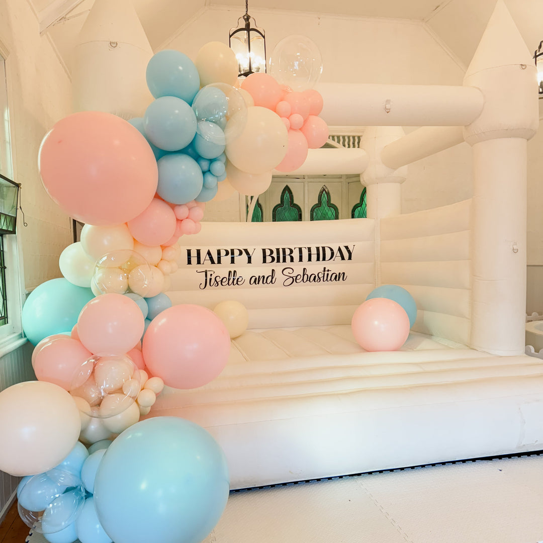 Angled view of the Jiselle pink, blue and clear balloon garland beside a Happy Birthday Jiselle and Sebastian decal