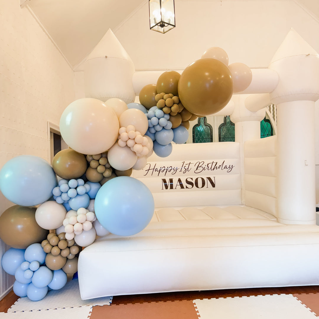 Angled view of the Mason caramel, blue and cream balloon garland beside a Happy 1st Birthday Mason decal under a lantern