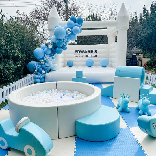 Baby blue soft play and round ball pit in front of a white castle with a blue balloon garland for party hire in Melbourne
