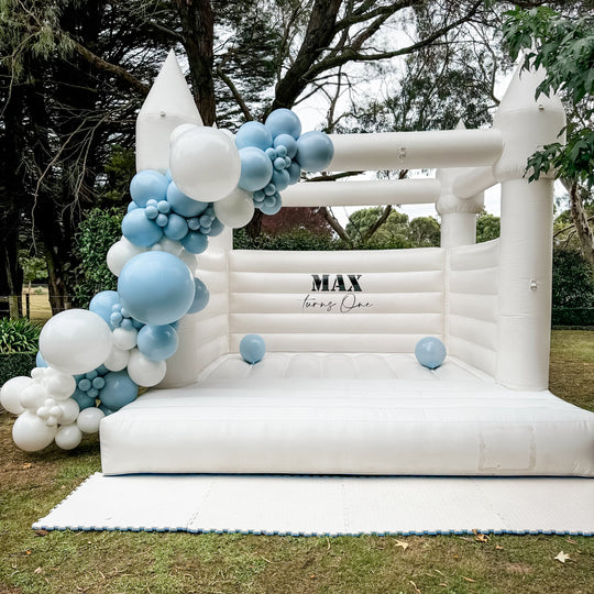 Max blue and white balloon garland on a white turreted bouncy castle with a Max turns One decal for party hire in Melbourne