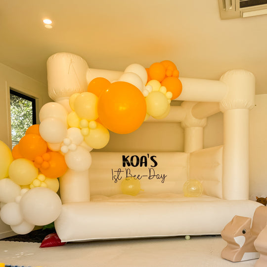 Koa orange and yellow balloon garland on a white bouncy castle with a Koa's 1st Bee-Day decal for party hire in Melbourne