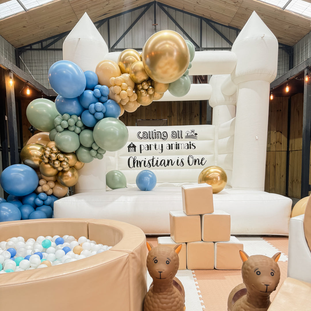 Alex white bouncy castle with a sage, blue and gold balloon garland and Calling all party animals Christian is One decal