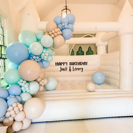 Jack and Lenny blue, sage and beige balloon garland on a white turreted bouncy castle in a chapel for party hire in Melbourne