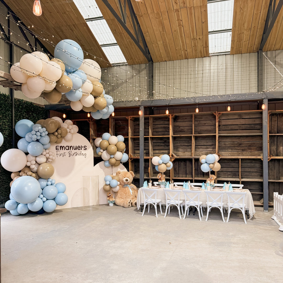 Wide view of the warehouse venue with garland on an arch and ceiling beam, teddy bears and a kids table with white chairs