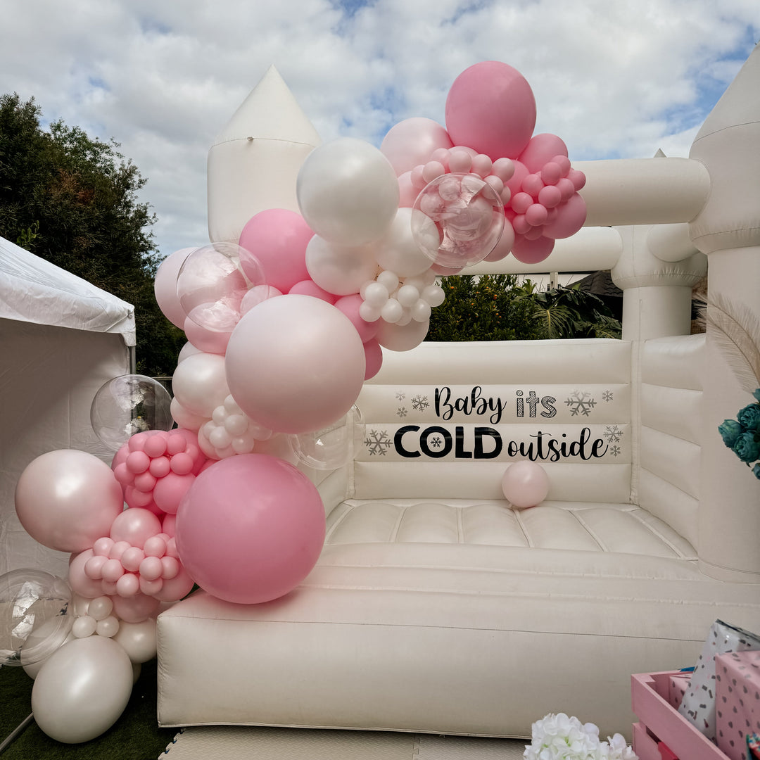 Bella balloon garland in pink, blush and white on a white bouncy castle with a Baby its Cold outside decal for party hire in Melbourne