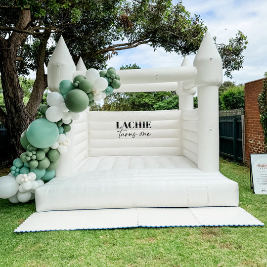 Lachie sage green and white balloon garland on a white turreted bouncy castle on a backyard lawn for party hire in Melbourne