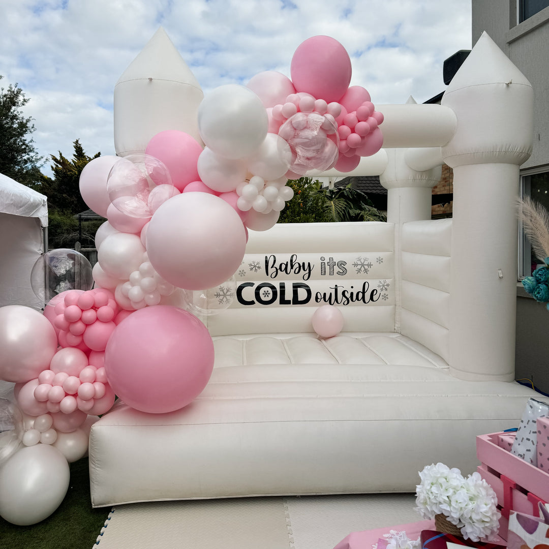 Bella balloon garland of pink, blush, white and clear balloons draped over a white bouncy castle tower with a snowflake decal