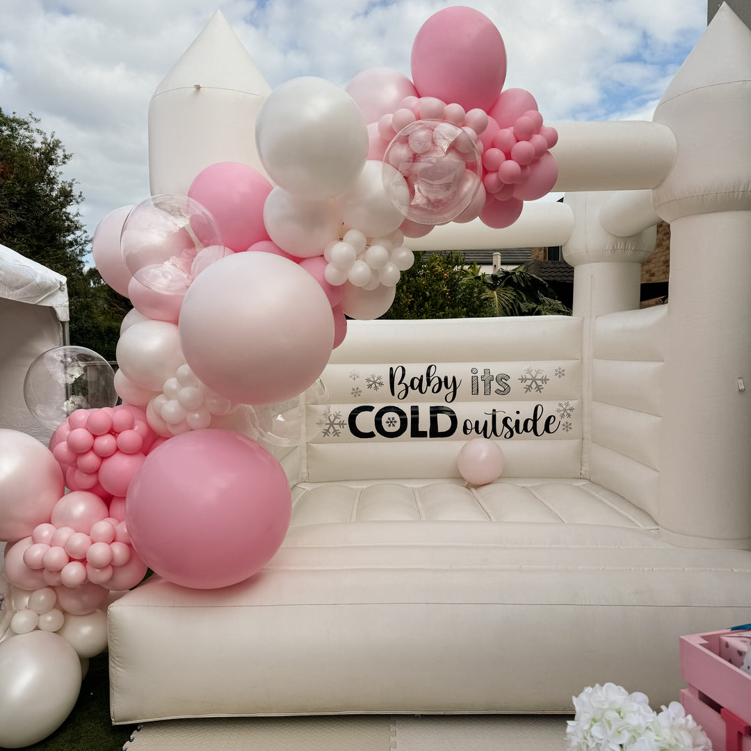 Bella balloon garland in pink, blush and white cascading down a white bouncy castle beside a snowflake decal and a pink crate