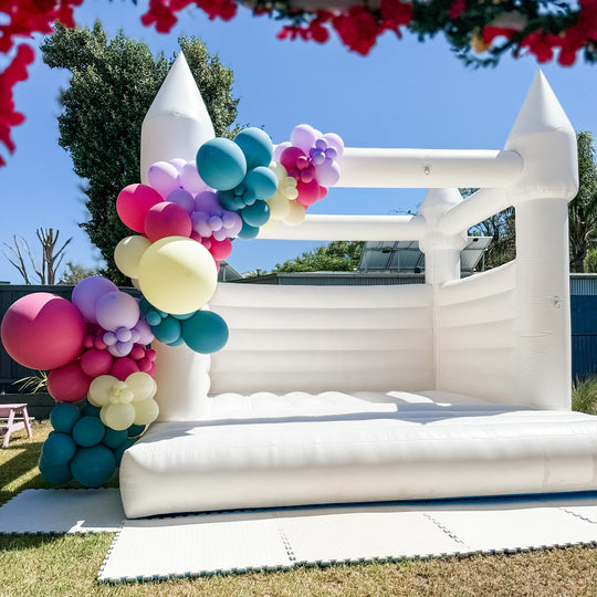 Trolls balloon garland in teal, hot pink, lilac and lemon on a white castle on a backyard lawn for party hire in Melbourne