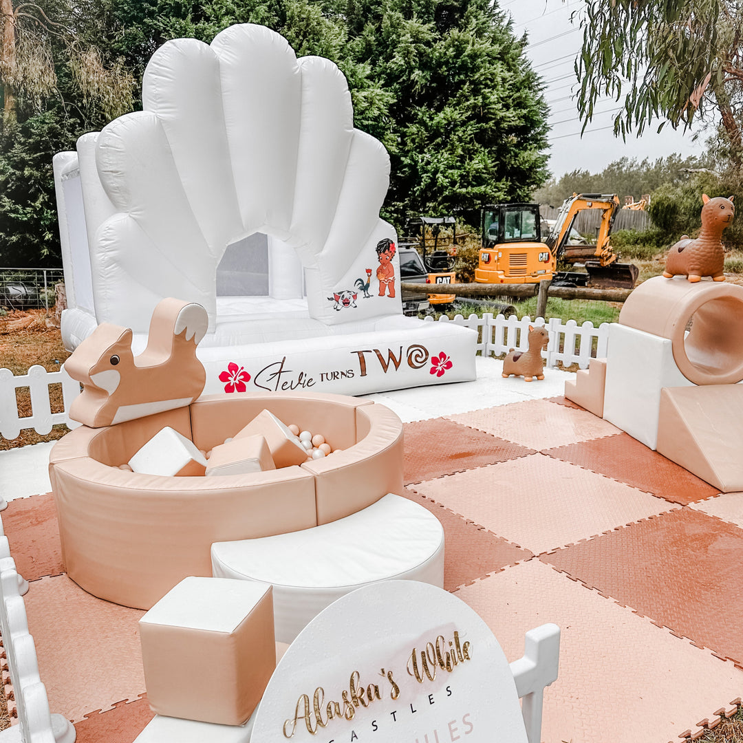 Moana themed Ocean shell castle with a Stevie turns two decal, tan soft play, round ball pit and rockers on peach mats