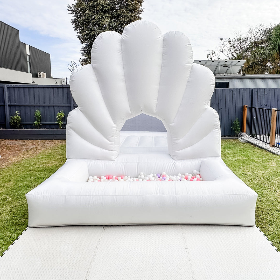 Ocean shell bouncy castle behind tan and white soft play blocks, a tunnel, ride-on car and ball pit inside a warehouse venue
