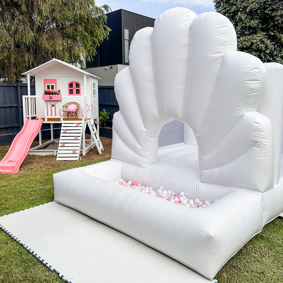 Ocean white shell shaped bouncy castle with a built-in ball pit of pastel balls on a lawn for party hire in Melbourne