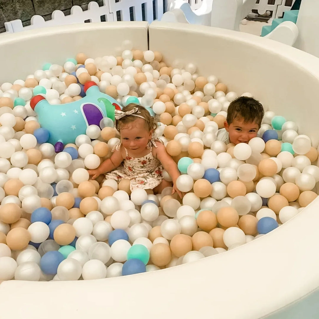 Two children sitting in the Elsa white ball pit filled with white, tan, blue and mint balls with a blue inflatable hopper toy