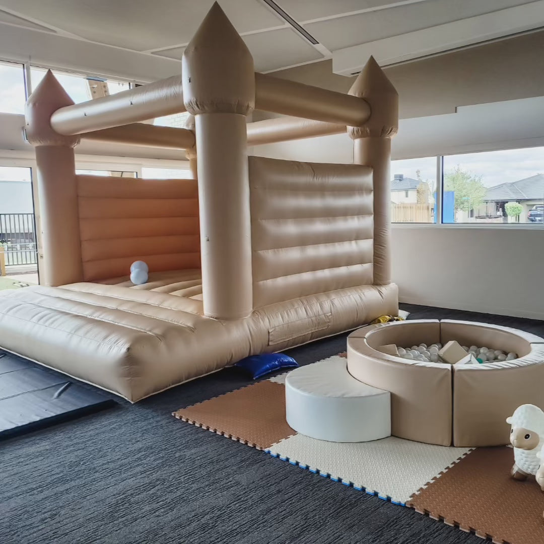 Summer tan bouncy castle and tan round ball pit with a white step and plush lamb toy on cream and tan foam mats indoors