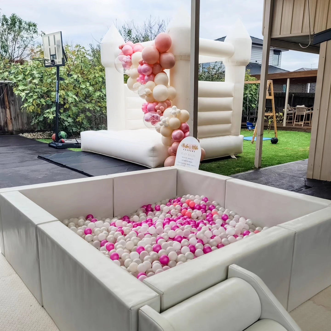 Olaf luxe white ball pit with white and hot pink balls on a paved patio with a white bouncy castle and pink garland behind