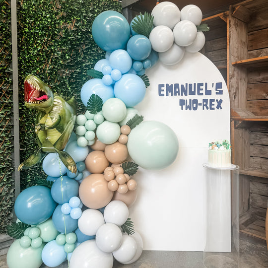 Acrylic cylinder plinth with a dinosaur cake beside an Emanuel's Two-Rex arch and blue balloons for party hire in Melbourne