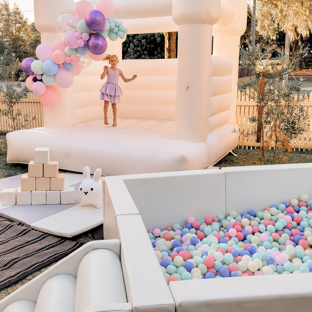 Olaf luxe white ball pit full of pastel balls beside a white bouncy castle and soft play blocks for party hire in Melbourne