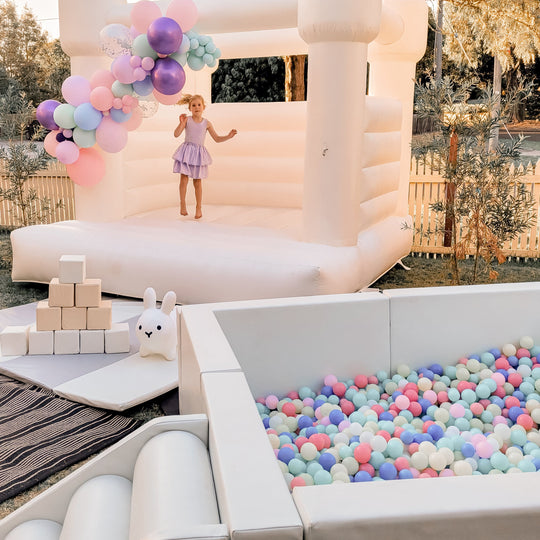 Olaf luxe white ball pit full of pastel balls beside a white bouncy castle and soft play blocks for party hire in Melbourne