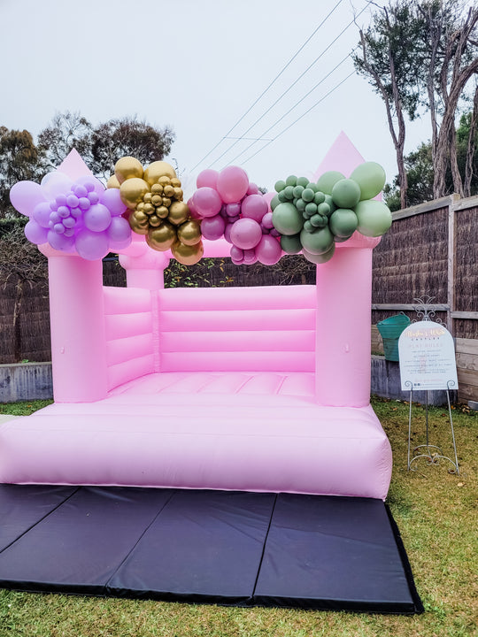 Pixy balloon garland in lilac, gold, rose and eucalyptus green on top of a pink bouncy castle for party hire in Melbourne