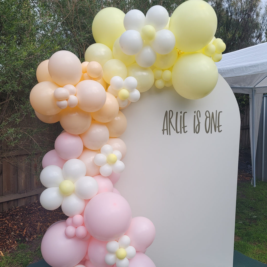 Arlie balloon garland in pastel yellow, peach and pink with daisy balloons on a cream Arlie is One arch for party hire in Melbourne