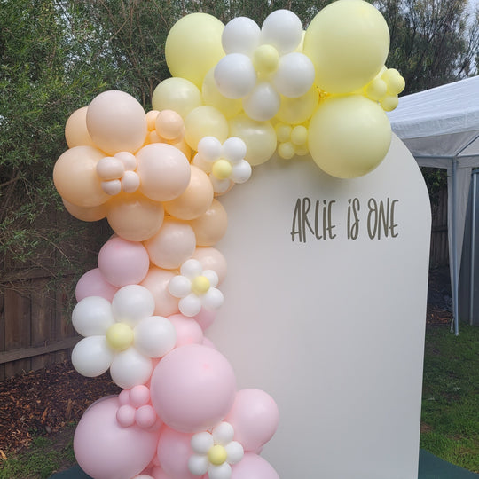 Arlie balloon garland in pastel yellow, peach and pink with daisy balloons on a cream Arlie is One arch for party hire in Melbourne