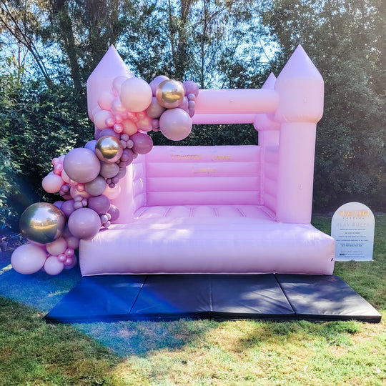 Princess pink bouncy castle with a pink, mauve and chrome balloon garland on a backyard lawn for party hire in Melbourne