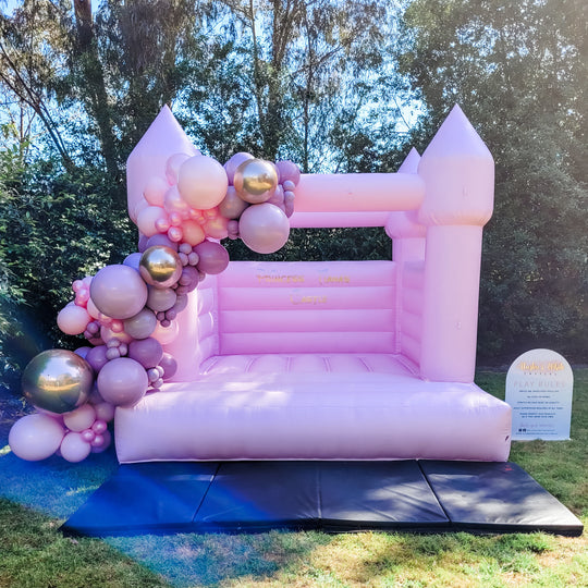 Princess balloon garland in blush, mauve and chrome gold draped over a pink bouncy castle for party hire in Melbourne