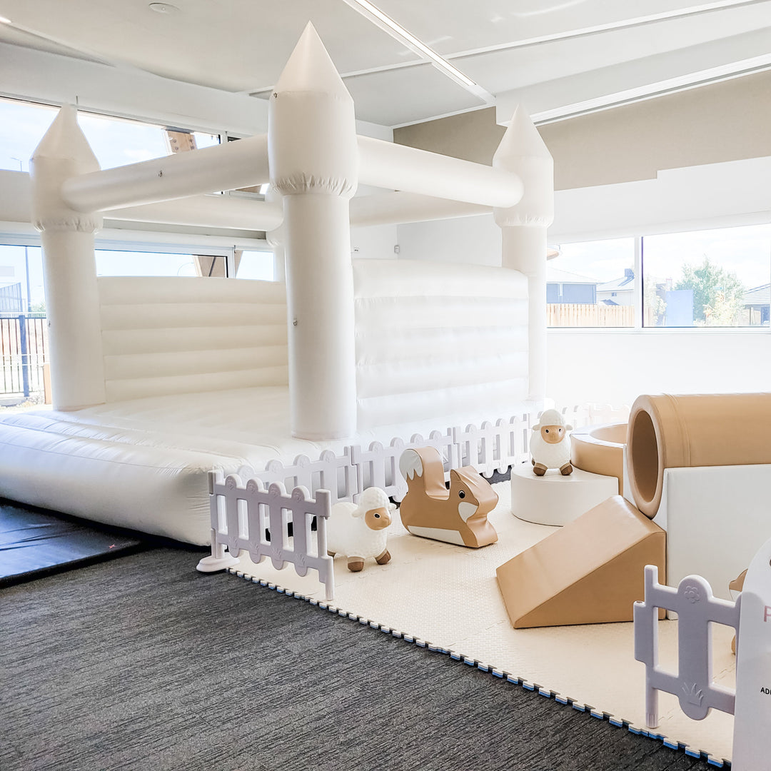 Alaska white castle indoors with neutral soft play, a white picket fence, sheep and fox rockers, a tan tunnel and a wedge