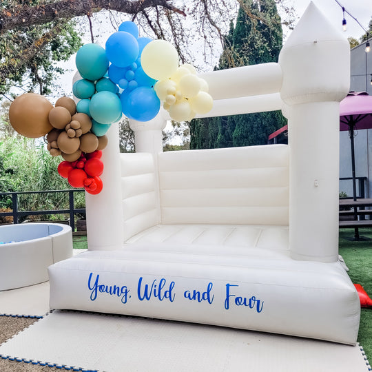 Billy balloon garland in tan, teal, blue and red on a white bouncy castle with a Young, Wild and Four decal for party hire in Melbourne
