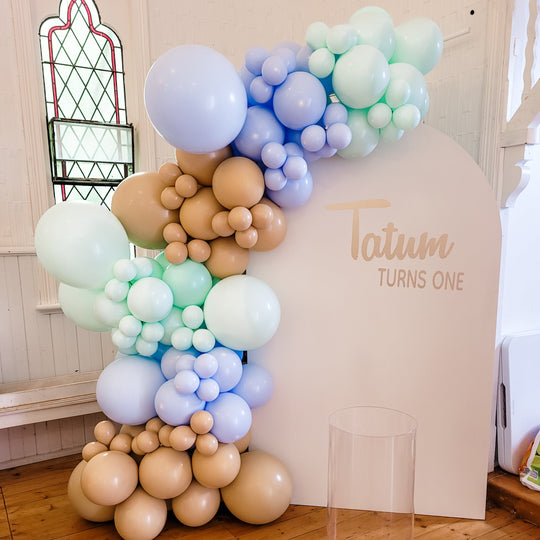 Tatum balloon garland in lilac, mint, pale blue and tan on a cream arch reading Tatum turns one for party hire in Melbourne