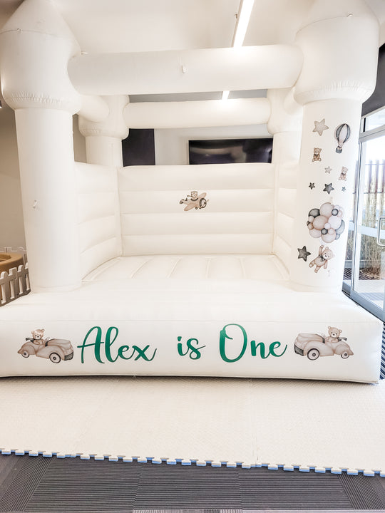 Teddy bear theme decals on a white bouncy castle with a green Alex is One decal in an indoor hall for party hire in Melbourne