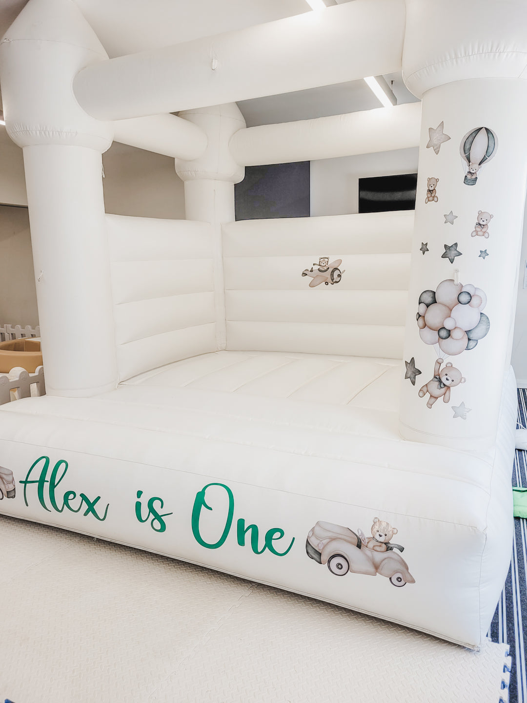 Angled view of the teddy bear balloon and star decals on a castle pillar beside the green Alex is One decal