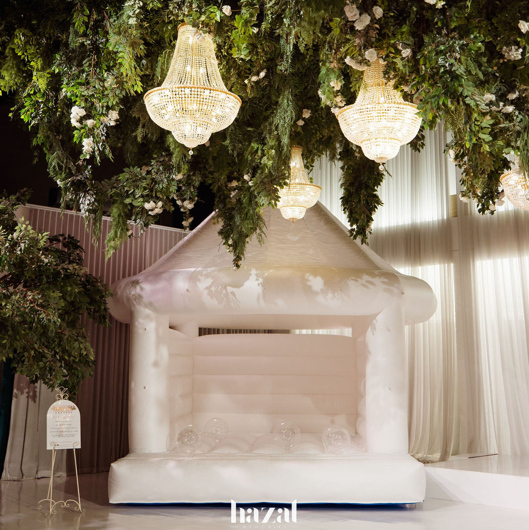 Dome white wedding bouncy castle under crystal chandeliers and hanging greenery indoors, for party hire in Melbourne