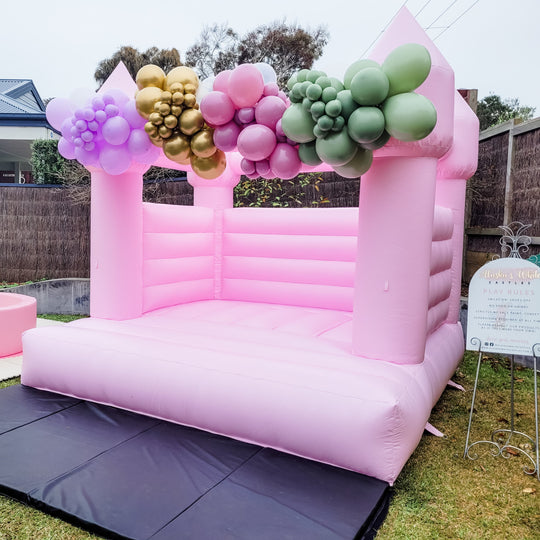 Pixy balloon garland in lilac, gold, rose and sage green across a pink bouncy castle outdoors for party hire in Melbourne
