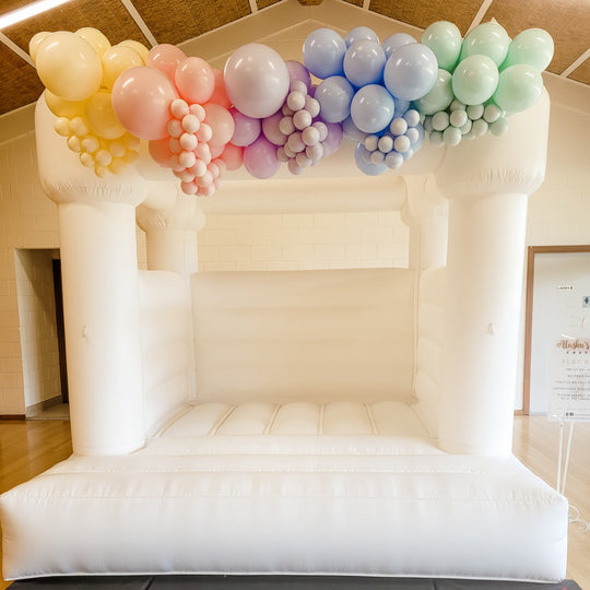 Pastel rainbow balloon garland in yellow, peach, lilac, blue and mint on a white bouncy castle for party hire in Melbourne