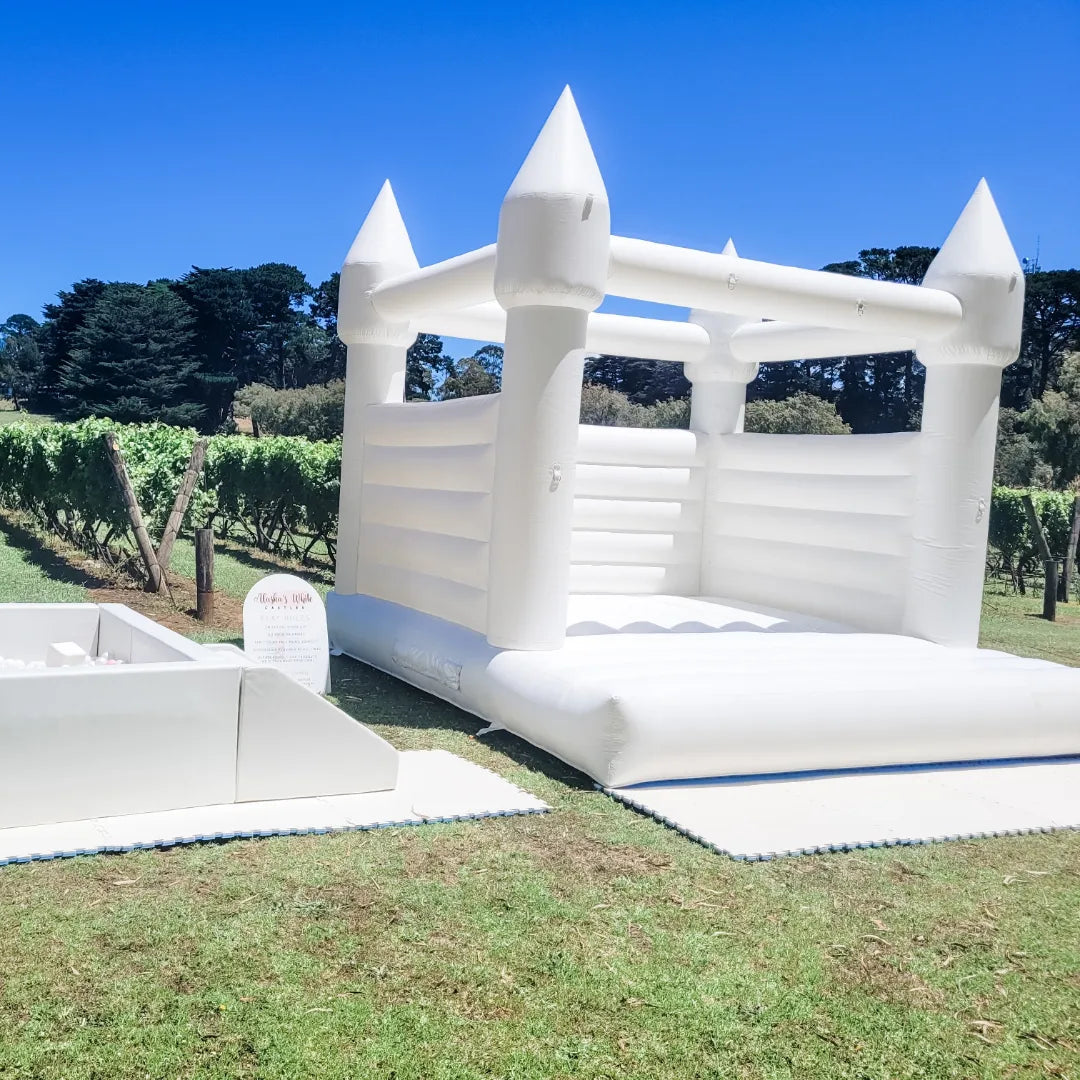 Alaska white bouncy castle and a white ball pit with entry steps on grass at a vineyard with a play rules sign and pine trees